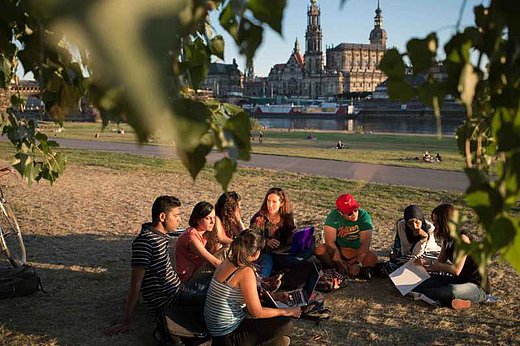 A group of students sitting by the river on a sunny late afternoon, Dresden skyline in the background