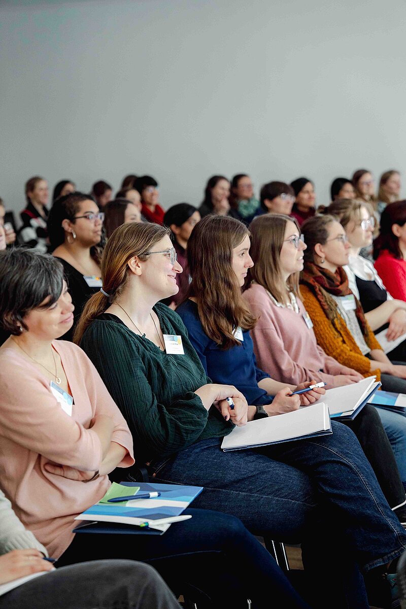 A crowd of scientists are sitting smiling and facing a presentation that is not visible to the right