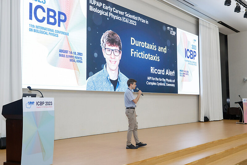 Scientist at the stage giving a speech and on the background a slide with his contribution 