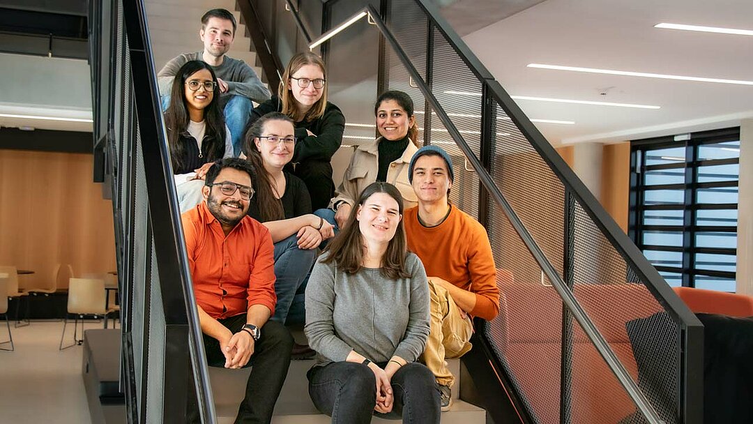 Eight people sitting on stairs in the atrium of a modern scientific institute