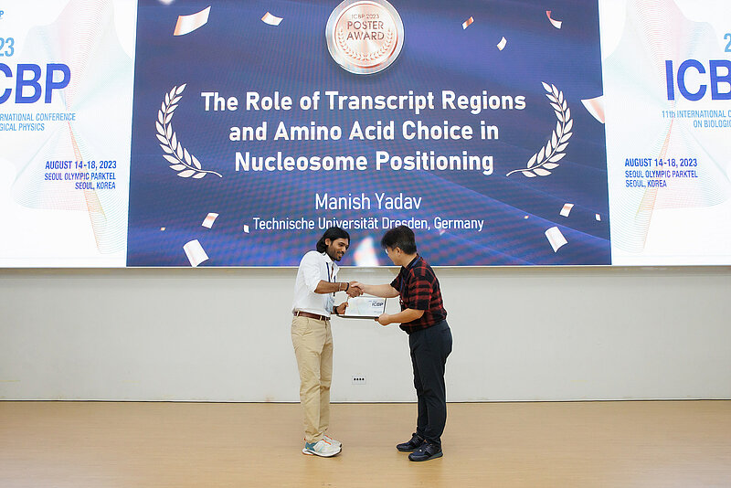 Two people shaking hands and holding a certificate on the foreground and on the background a slide explaining the prize