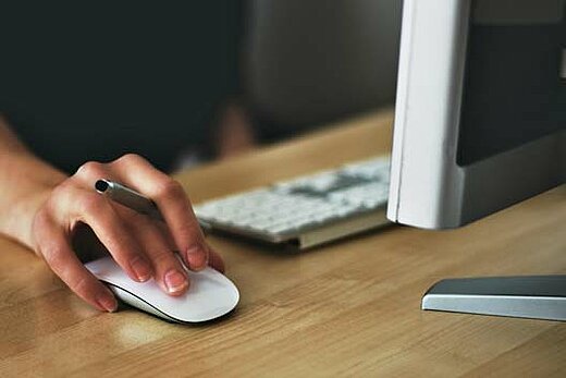 Close-up of a hand using a computer mouse with parts of a computer display and keyboard visible on a desk