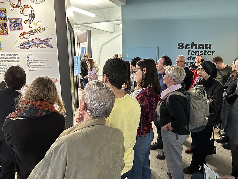 A large crowd of people are visiting a museum exhibition - many people stand around one exhibit showing some text and illustrations of zebrafish. 