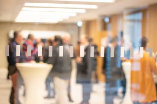 People in the vestibule near conference rooms during a break, seen blurry through a window pane