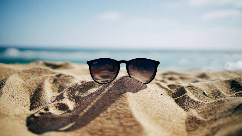 A pair of sunglasses on a heap of sand on the beach, the sea in the background, shot in the late afternoon sun