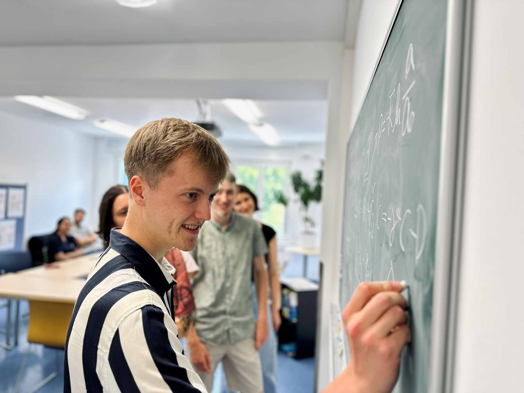 Students in front of a blackboard, one of them writing on it